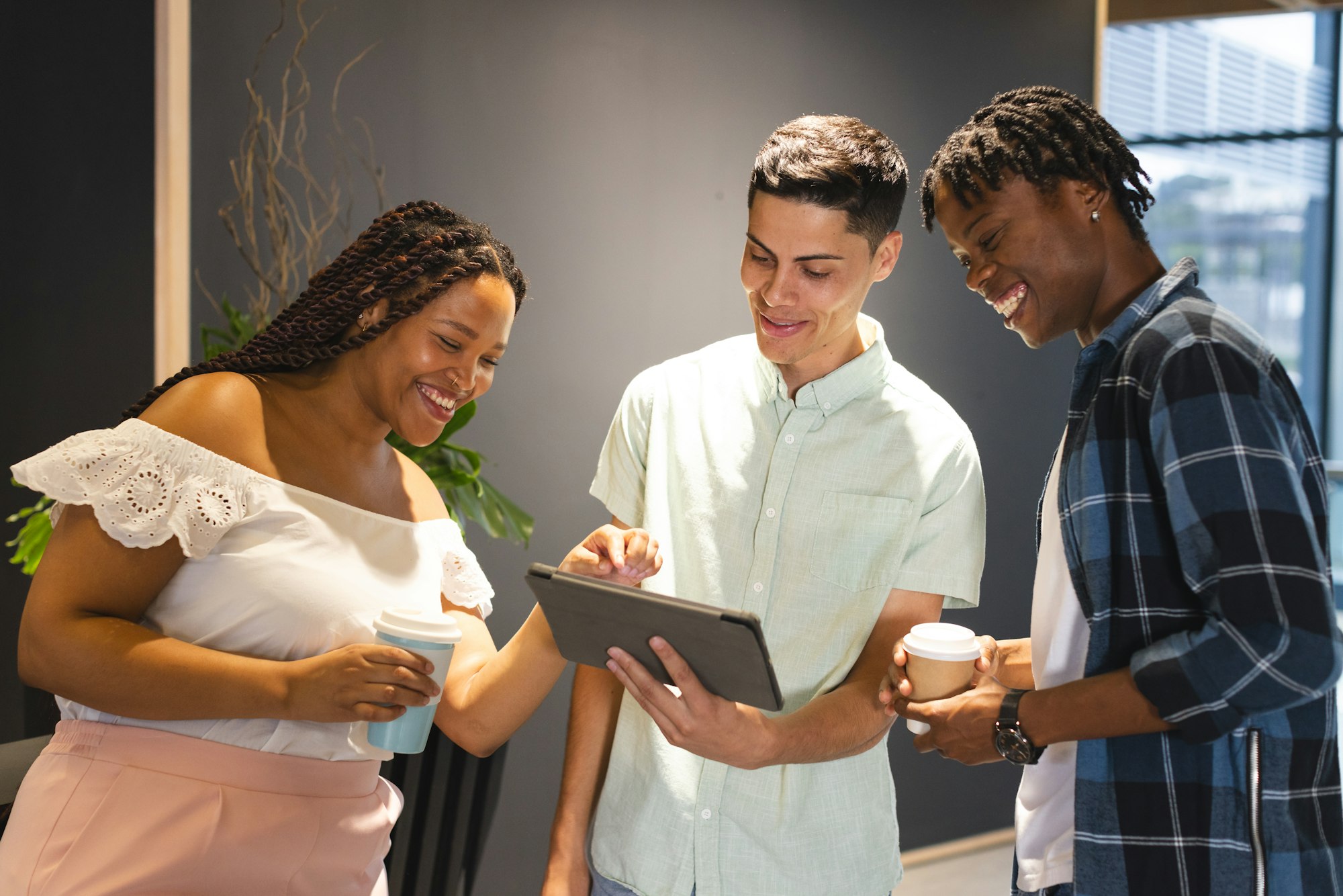 A diverse group of colleagues sharing a tablet and laughing together in a modern business office