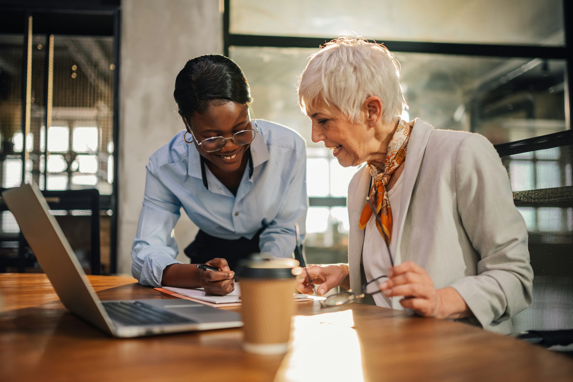 Interracial employee with textbook consulting senior businesswoman.